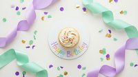 Festive birthday cupcake with colorful sprinkles on a card, surrounded by pastel ribbons and confetti on a white background.