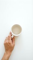 Hand holding an empty white ceramic mug from above on a white background, minimalist flat lay concept for coffee or tea lifestyle.