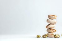Stack of roasted salted pistachios balanced on white background, with scattered open shells and kernels creating minimalist composition for food styling.