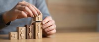 Businessman building wooden blocks with family icons showing growth and protection concept for life insurance and family planning strategies.