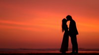 Romantic couple silhouette embracing at sunset beach with orange sky. Love, romance, relationship concept for wedding, anniversary, Valentine's Day designs.