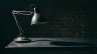 Vintage desk lamp with articulated arm casting dramatic shadow on wooden surface against dark brick wall background for workspace design.