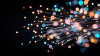 Glowing fiber optic strands with orange and blue bokeh lights against black background create dynamic movement and energy effect for technology designs.