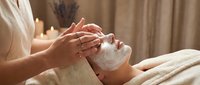 Young woman receiving relaxing facial massage treatment at luxury spa with healing hands and serene candlelit atmosphere for wellness and self-care.