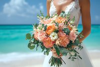 Bride holding luxurious coral and peach wedding bouquet with roses, peonies, and eucalyptus against turquoise ocean water and tropical beach background.