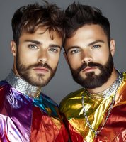 Two bearded men in vibrant metallic jackets with sequin collars pose together against gray background. Fashion portrait showcasing modern LGBTQ+ style and pride concept.