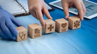 Doctor arranging wooden blocks with healthcare icons including stethoscope, pharmacy, and medical symbols on blue desk surface for hospital management.