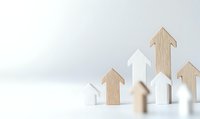 Wooden and white house-shaped blocks with arrow figures symbolizing growth, progress and real estate market trends on clean white background.