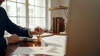 Professional businessman stamping documents at wooden desk in bright office with books and papers for legal approval and business certification processes.