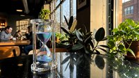 Modern office workspace with hourglass timer and green plants on reflective desk surface creating productive work environment for business professionals.