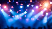 Blurred concert lighting with vibrant blue and pink bokeh effects creates atmospheric stage background. Bright spotlight beams pierce through smoky atmosphere.