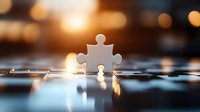 Single white puzzle piece standing upright on reflective surface with warm bokeh lights in background, creating dramatic lighting and depth for business concepts.