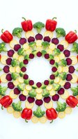 Colorful vegetable mandala pattern with red bell peppers, broccoli, beetroot and potato slices arranged in circular design on white background.