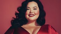 Young Asian woman with dark wavy hair and red lipstick smiling confidently against pink background, wearing red dress. Professional beauty portrait showcasing plus size fashion model.