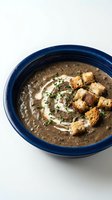Creamy mushroom soup served in a blue bowl, topped with golden croutons, fresh herbs, and a drizzle of cream. Perfect for restaurant menus, food blogs, and culinary publications.
