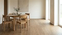 Modern minimalist dining room with wooden table and chairs on light hardwood floors featuring natural sunlight from large windows.