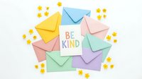 Colorful pastel envelopes arranged around a Be Kind greeting card with small yellow flowers on white background, flat lay composition.