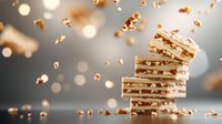 White chocolate bars stacked with crushed nuts and caramel pieces scattered against blurred bokeh background, dramatic food photography with warm tones and selective focus.