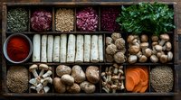 Fresh ingredients in rustic wooden box compartments featuring mushrooms, herbs, spices, carrots and legumes arranged in culinary composition for cooking preparation.
