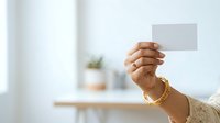 Close-up of a woman's hand holding a blank white card or note in a bright, minimalist interior space. Suitable for business, marketing, and communication concepts.