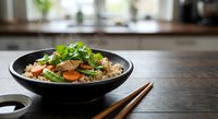 Asian fried rice with vegetables and herbs in black bowl on wooden table with chopsticks in modern kitchen setting for cooking and dining concepts.