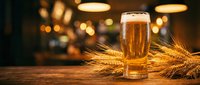 Golden beer glass with foam on wooden table surrounded by wheat stalks in warm pub atmosphere with blurred lights creating cozy ambiance for brewing concepts.