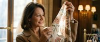 Middle-aged woman with dark hair examining a floral patterned garment in an upscale boutique setting, evaluating fabric quality and design for retail or fashion consultation purposes.