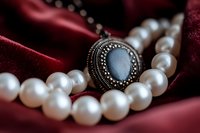 Elegant pearl necklace with vintage silver pendant featuring blue gemstone on luxurious burgundy velvet fabric, macro jewelry photography for fashion and luxury accessories.