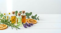 Natural essential oils in glass bottles with cork stoppers, dried orange slices, lavender, rosemary and eucalyptus leaves for aromatherapy and wellness.