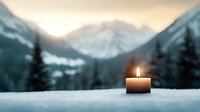 Glowing candle in snow against majestic mountain landscape at dusk, creating atmospheric winter mood with soft bokeh and warm candlelight against cold scenery.