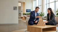 Professional business team building wooden blocks together in modern office space representing teamwork and strategic planning concepts.