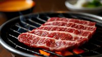 Sliced raw beef marbling on hot grill grates with flames, ready for cooking. Use for restaurant menus, food blogs, barbecue promotions, and culinary content.