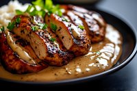 Juicy sliced chicken breast with creamy mushroom sauce garnished with fresh herbs on dark plate, close-up view showing moist texture and caramelized surface.