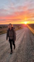 Woman jogging on rural dirt road at golden hour sunset with vibrant orange and yellow sky, rolling hills landscape, outdoor fitness and exercise activity.