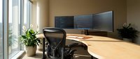 Modern office workspace with curved wooden desk, ergonomic chair and triple monitor setup for productivity and professional work environment.