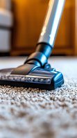 Close-up view of vacuum cleaner head on beige carpet showing detailed texture and cleaning process. Modern appliance with metallic blue accents in home setting.