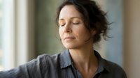 Peaceful middle-aged Caucasian woman with closed eyes practicing mindfulness meditation indoors. Serene moment of relaxation and mental wellness at home.