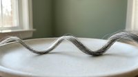 Wavy metallic wire twisted into undulating curves on white surface, suitable for abstract design, product visualization, and creative backgrounds.