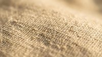 Natural burlap fabric texture with coarse weave pattern in warm beige tones, close-up macro photography showing detailed fiber structure for rustic design projects.
