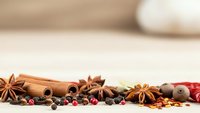 Aromatic spices including cinnamon sticks, star anise, peppercorns and cardamom arranged on wooden surface for cooking and baking recipes.
