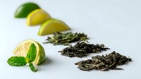 Fresh lime slices and mint leaf arranged with piles of loose-leaf tea on white background, showcasing ingredients for herbal infusions.