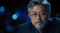 Professional mature Asian businessman with glasses and gray hair in dark suit against blurred city lights background for corporate and executive concepts.