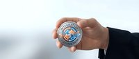 Hand holding commemorative coin with medical cross symbol and circular text design against blurred background for healthcare finance concepts.