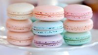Pastel colored French macarons in soft pink, mint green and baby blue shades arranged on white plate, sweet meringue based cookies with cream filling.