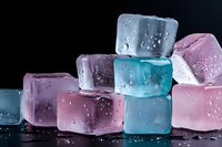 Colorful ice cubes in pink and blue tones with water drops on black background, macro shot showing frozen crystal structure and melting surface texture.