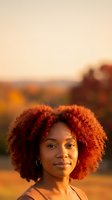 Young African American woman with vibrant curly afro hair enjoying golden hour sunset light outdoors with warm glowing background for lifestyle content.