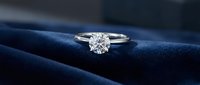 Elegant diamond solitaire engagement ring with brilliant cut stone on luxurious navy blue velvet fabric background for wedding and jewelry concepts.