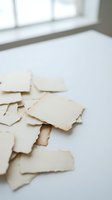 Torn vintage paper pieces scattered on white surface near window creating artistic composition for creative projects and design work.