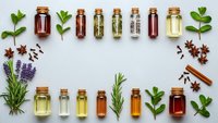 Essential oils in amber glass bottles with fresh herbs and spices arranged in decorative frame on white background for aromatherapy and natural wellness.