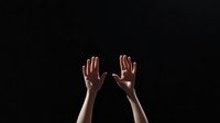 Two hands raised up against dark background showing palms in surrender or stop gesture for communication and body language concepts.